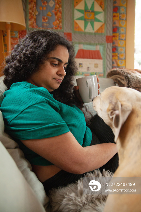 Curvy Indian girl with Cerebral Palsy drinking coffee next to her dog in the living room