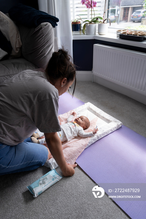 Mother bending over baby girl lying on changing mat at home