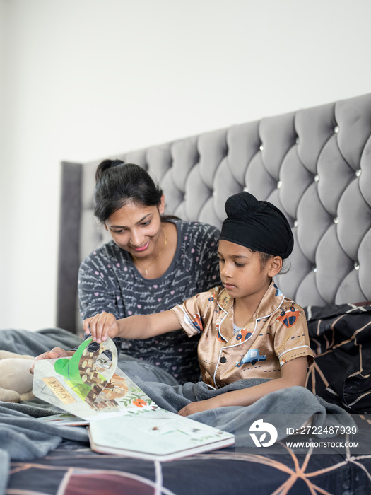 Mother and son (6-7) reading book in bed