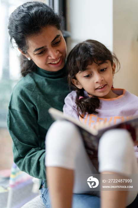 Mother and daughter sitting near window and reading book