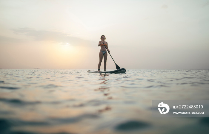 Woman paddleboarding on sunset sea