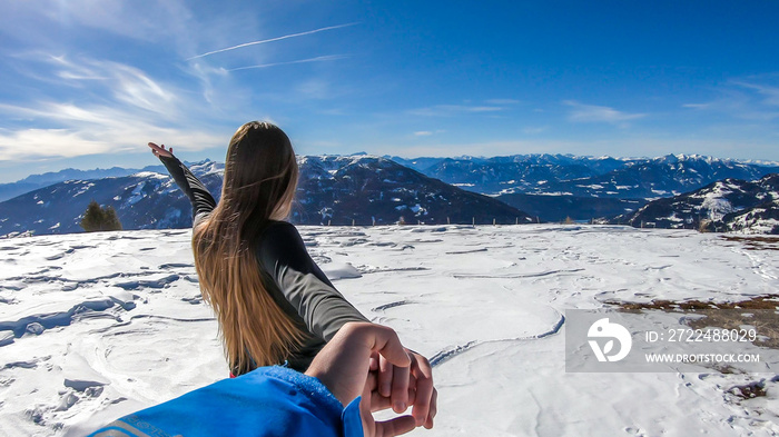 A girl holding a man’s hand on a snowy background in Bad Kleinkirchheim, Austria. Follow me to winter wonderland! She is happy, having fun. There is a lot of snow caped mountain in the back.