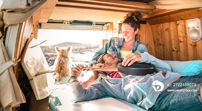 Hippie couple amd dog traveling together on vintage van transport at sunset - Life inspiration concept with guy and girl on minivan adventure trip with ukulele in relax moment - Warm sunshine filter