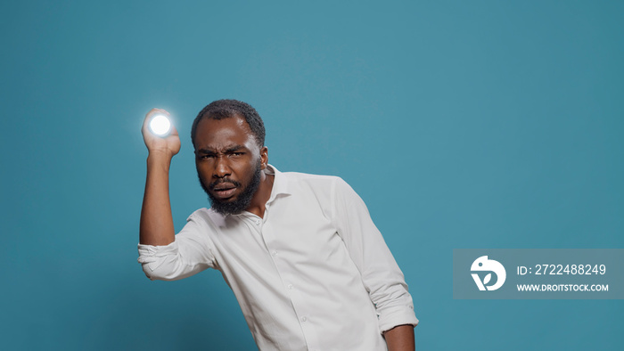 Scared man using lantern to make light and look around in studio, holding flaslight to search and examine dangerous creepy sound. Serious person with courage chasing and doing investigation.