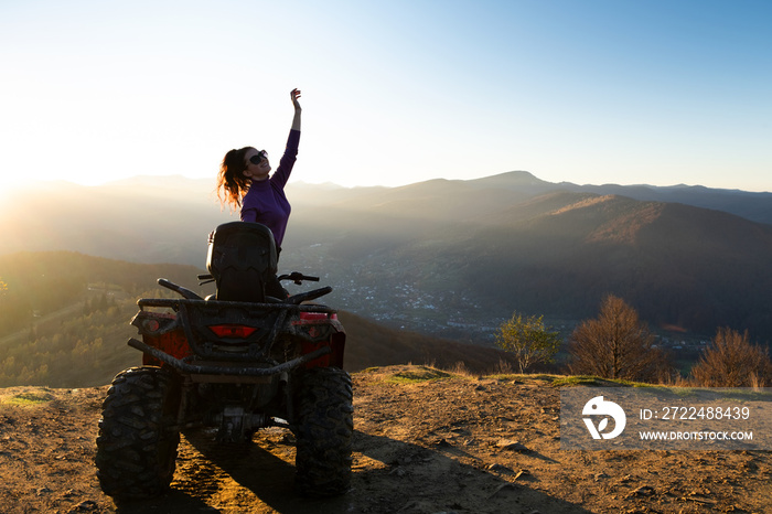 Young happy woman enjoying extreme ride on atv quad motorbike in autumn mountains at sunset.