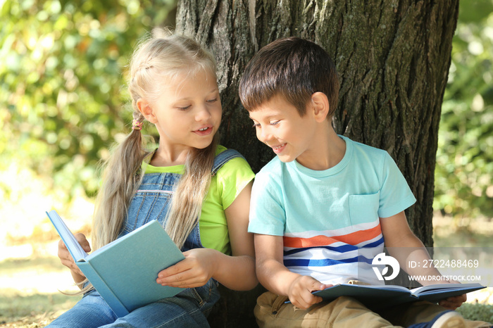 Cute little children reading books near tree in park