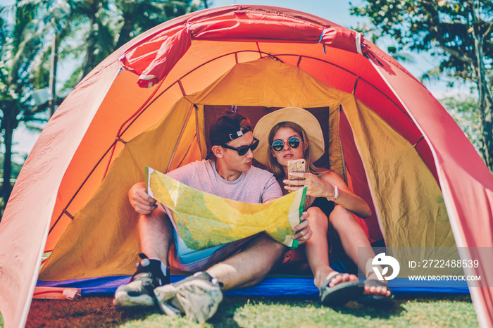 Young woman browsing information on smartphone reading travel blogs planning with boyfriend route for camping,hipster couple making research via cellular checking map direction resting in tent