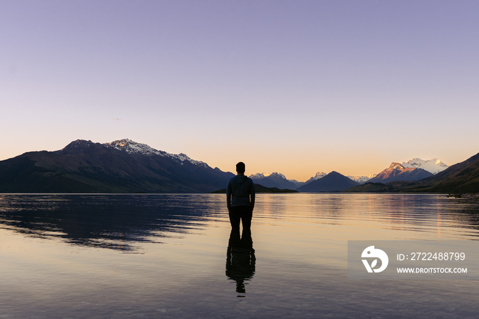 Man inside Lake Wakatipu looking at the amazing sunset behind snowy mountain peaks. New Zealand