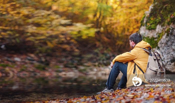 Travel and road trip concept at autumn. Adventure and active lifestyle in nature. Tourist hiking in forest. Caucasian man in yellow jacket walks in woods.