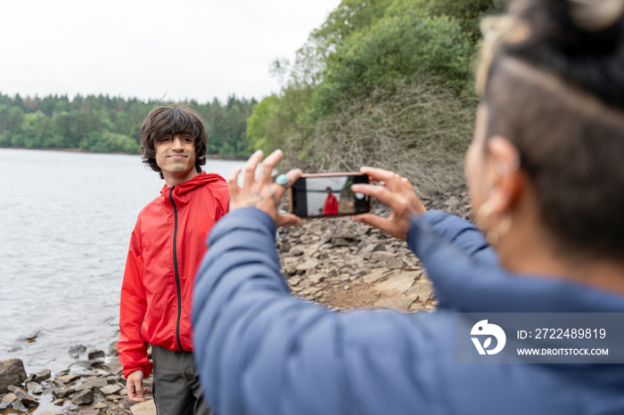 Mother photographing son by lake on hike