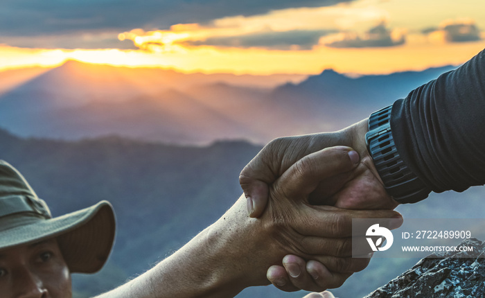 Two Male hikers climbing up mountain cliff and one of them giving helping hand. People helping and, team work concept.