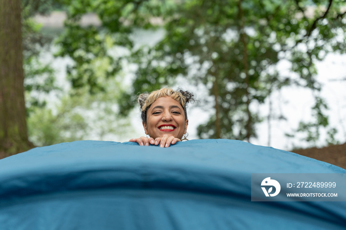 Smiling woman setting up tent in forest