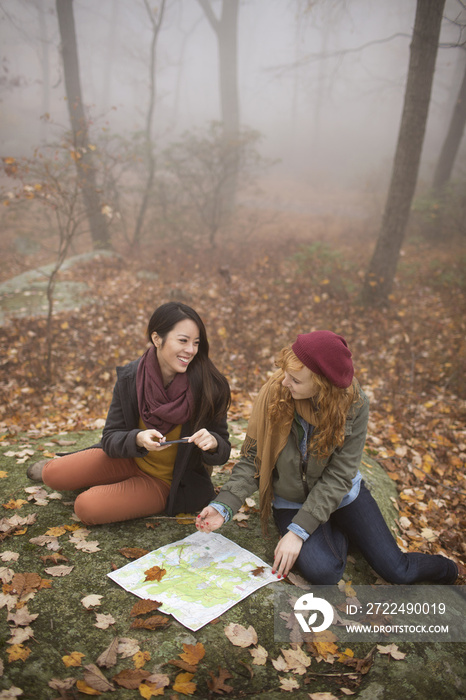 Friends with map sitting on rock in forest