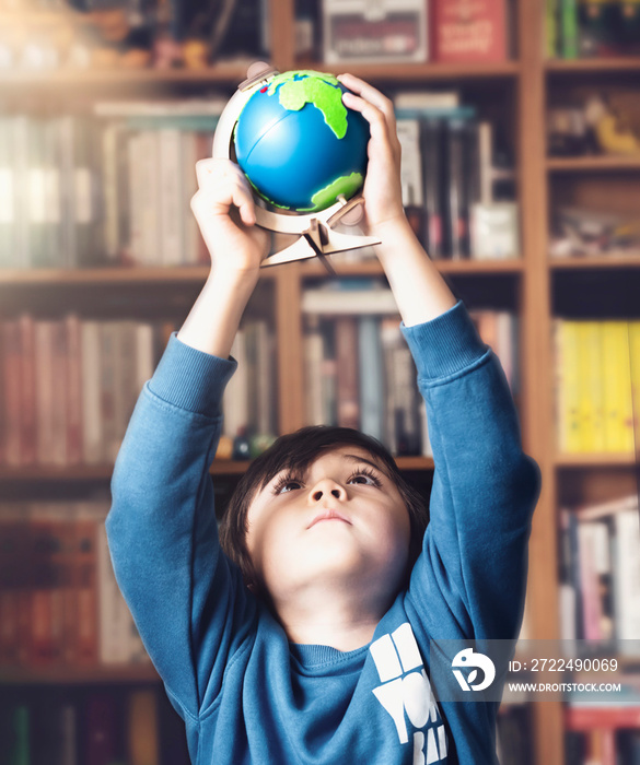 Portrait young kid holding globe high up over his head looking up from underneath with curious face, Child boy learning about Geography, Education and Homeschooling concept