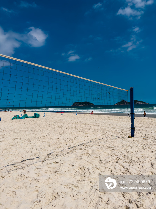 Volleyball net or futvolei on the sand of Barra da Tijuca beach, Rio de Janeiro, Brazil. Sunny day with blue sky and some clouds. Windsurfing at sea