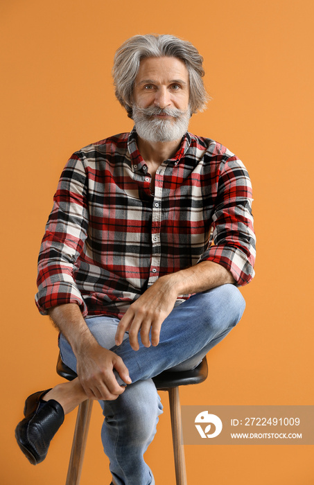 Portrait of handsome senior man sitting on chair against color background