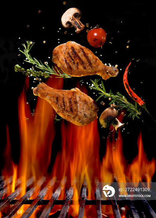 Chicken legs and spicy ingredients flying above flaming red barbeque grill