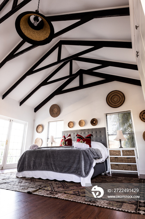 Bed with blankets and pillows and decorations hanging on mansard roof and wall in modern bedroom