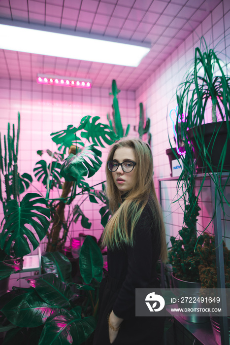 Portrait of a beautiful young girl in a room with neon violet light and vases.