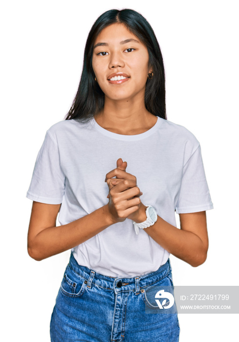 Beautiful young asian woman wearing casual white t shirt with hands together and crossed fingers smiling relaxed and cheerful. success and optimistic