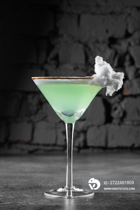 Green alcohol cocktail in a glass decorated with cotton candy on gray background.