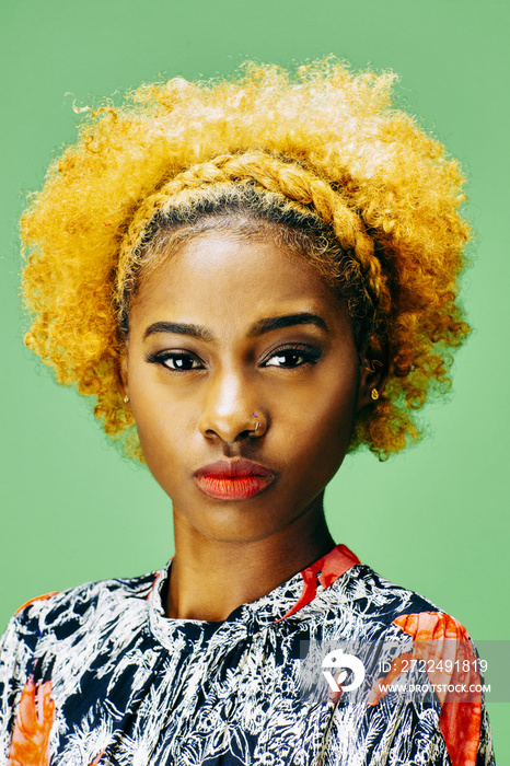 Vertical portrait of a lovely young girl with bleached curly hair, in front of a green background