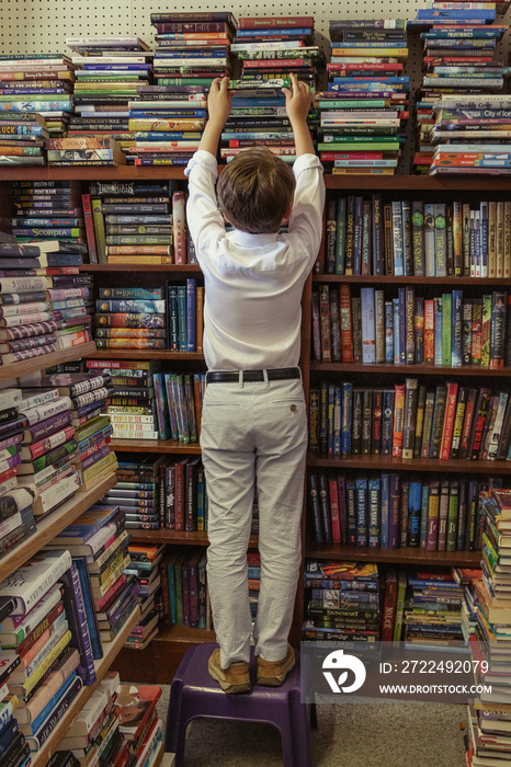 child with stack of books in store