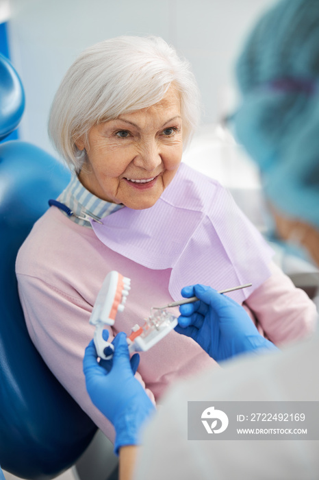 Interested pensioner looking at dentist with dental model