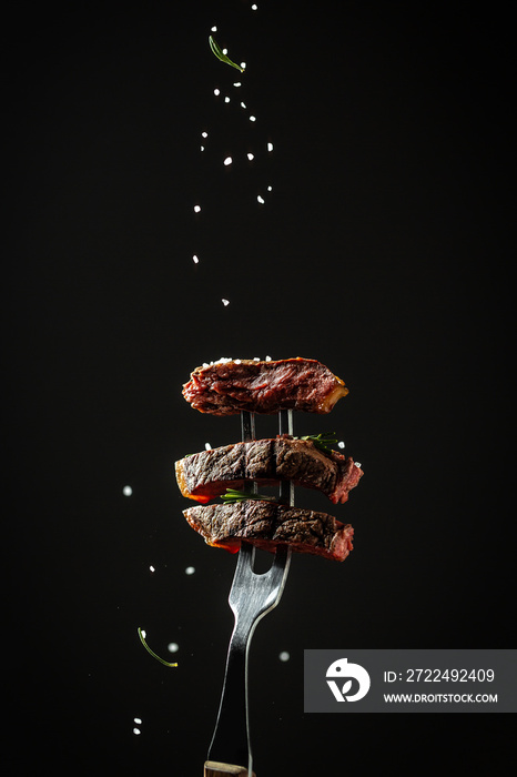 Traditional American barbecue dry aged flank steak sliced on a fork adding rosemary and sea salt in a freeze motion on black background. vertical image, American cuisine