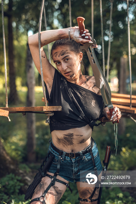 portrait of girl in torn clothes holding a knife and posing in the woods