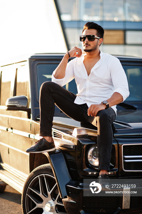 Solid asian man in white shirt and sunglasses posed near black mafia suv car.