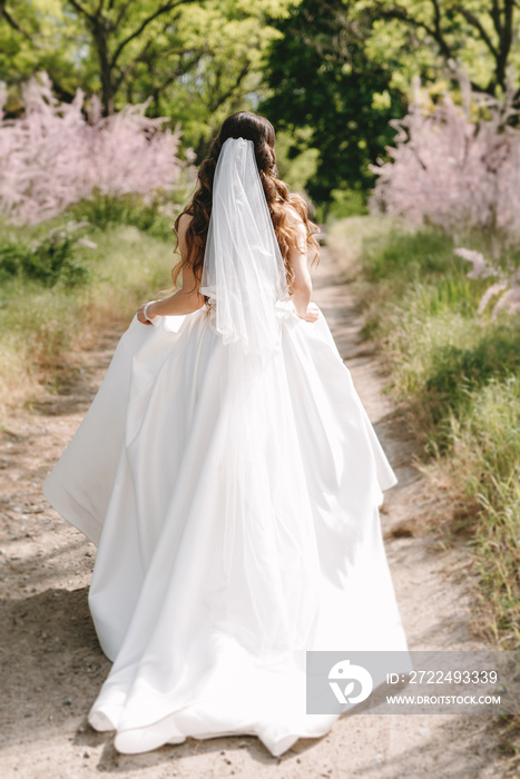 a young girl bride in a white dress is spinning on a path