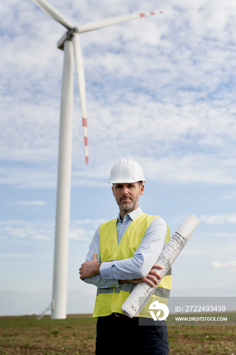 Portrait of caucasian engineer holding paper project while standing on wind turbine field