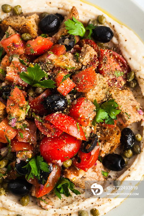 vegan panzanella salad on a layer of hummus on a plate. tasty healthy food.