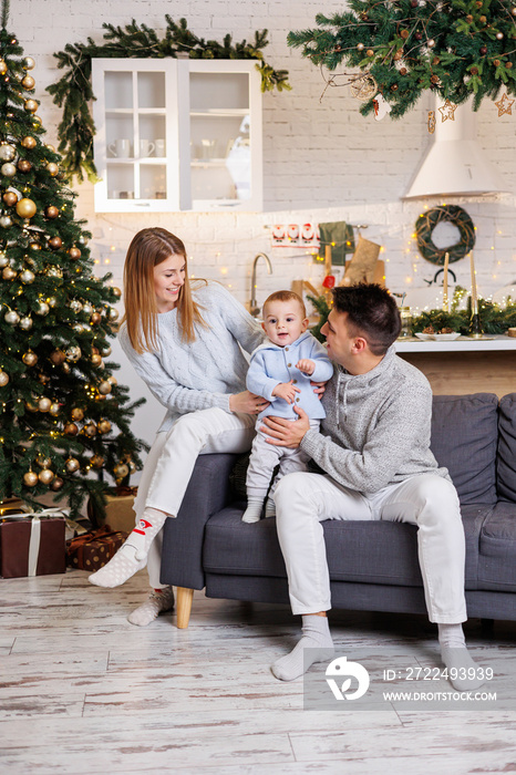 A happy family is sitting on the couch with their little son near the Christmas tree and smiling joyfully. Home festive atmosphere of the new year.