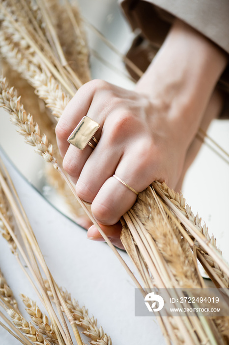 Cropped view of female hand with golden rings on fingers holding bunch of wheat