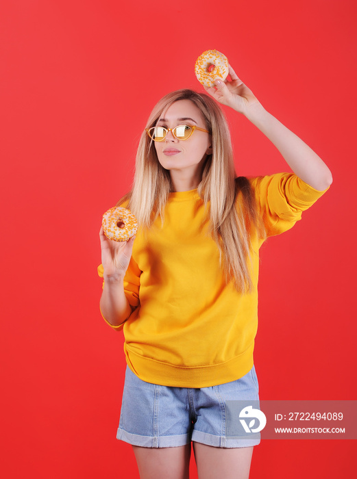 Smiling caucasian woman in yellow sweater with donuts posing on red background.