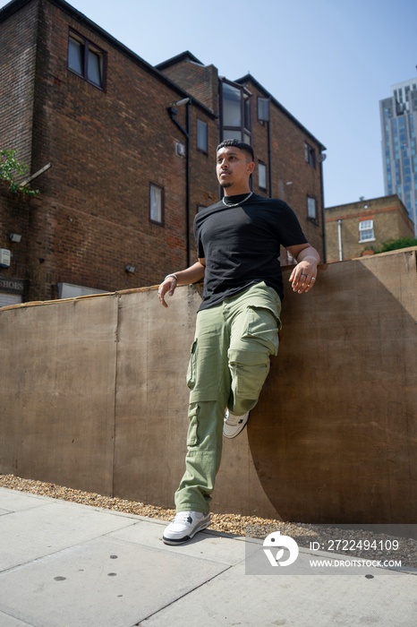 Man wearing back tshirt and cargo pants leaning on wall