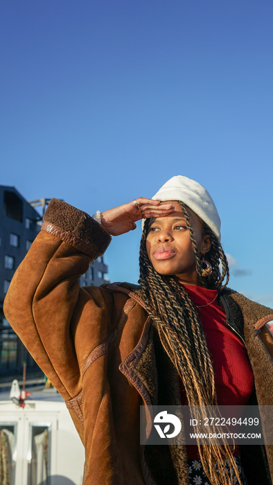 Young woman with braided hair and cap shielding eyes outdoors