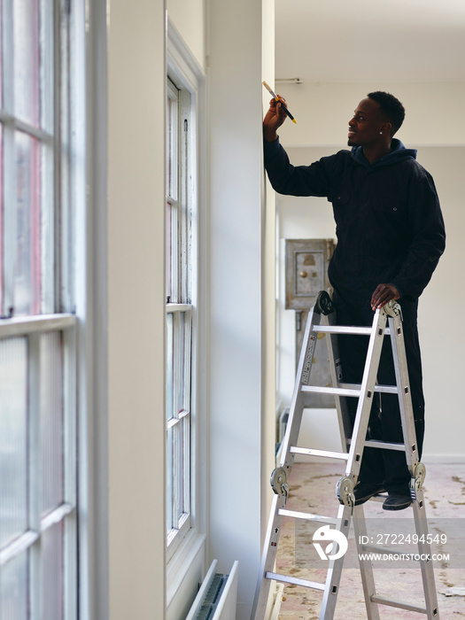 Man standing on ladder and painting house walls