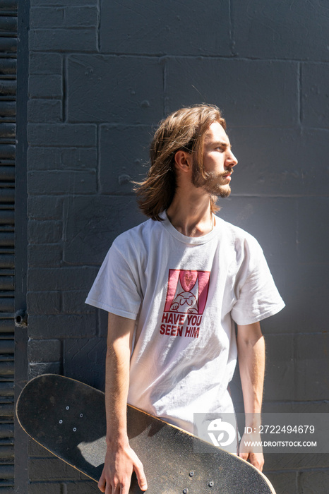 Young man standing outdoors holding skateboard