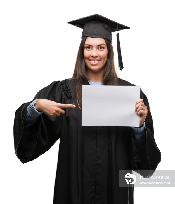 Young hispanic woman wearing graduated uniform holding diploma paper very happy pointing with hand and finger