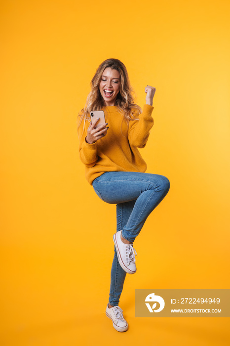 Full length image of delighted blonde woman rejoicing and holding cellphone