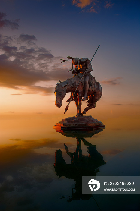 native american bronze sculpture in water at sunset