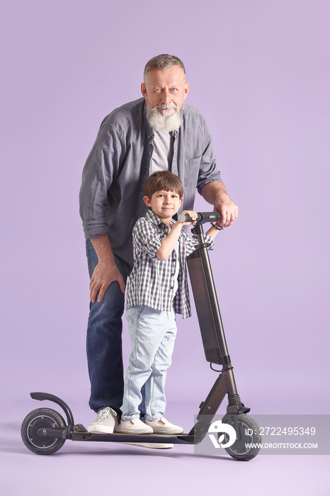 Cute little boy with kick scooter and his grandfather on color background