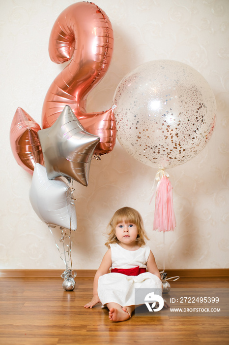 Little blonde baby girl two years old with big pink and white balloons on her birthday party