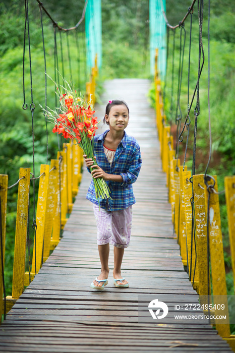 Teenage girl on footbridge with bunch of flowers, Shan State, Keng Tung, Burma