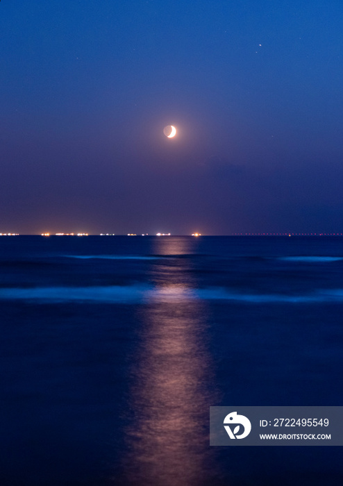 Vertical seascape with seasparkle and a waxing crescent moon in the sky.