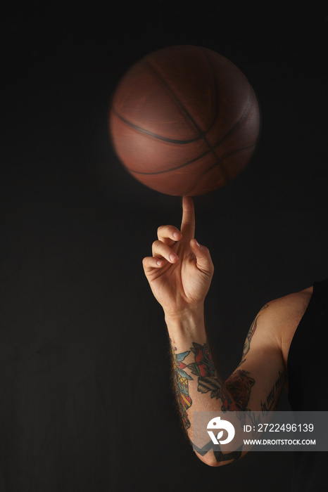 Leather basketball spins over on finger of tattooed athlete’s hand, isolated on black