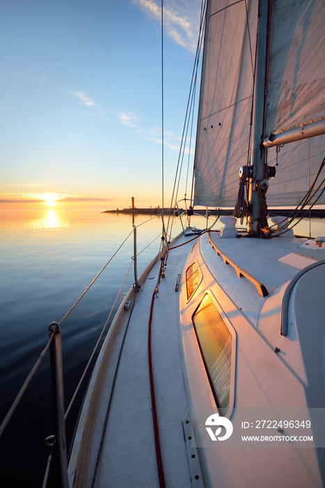 White yacht sailing after the rain at sunset. Close-up view from the deck to the bow. Clear blue sky with glowing clouds reflecting in a still water. Idyllic seascape. Sea, cruise, travel destinations